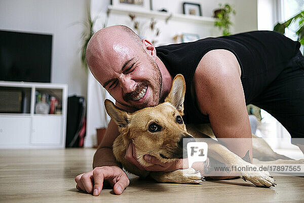 Happy man with eyes closed embracing pet dog at home