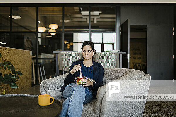 Young businesswoman eating healthy snack sitting in cafeteria at office
