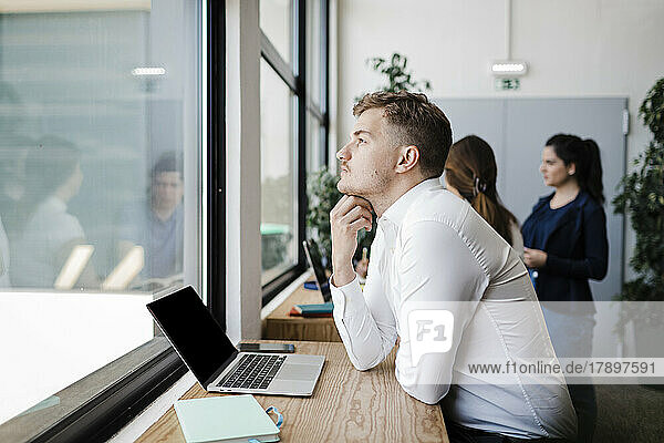 Contemplative businessman with laptop looking out of window