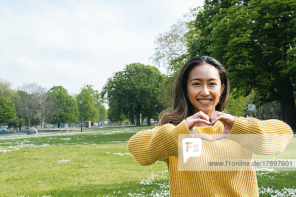 Glückliche junge Frau formt im Park mit den Händen ein Herz