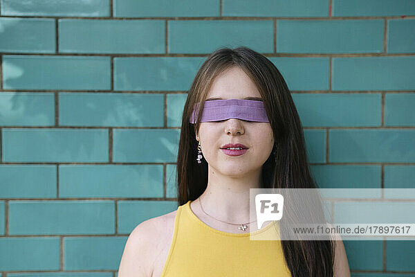 Woman with blindfold in front of teal wall