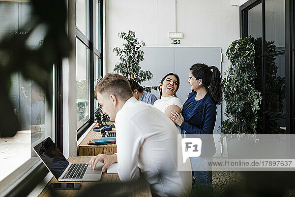 Happy businesswoman with colleagues working on laptop in office