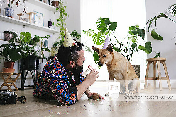 Man with sausage looking at pet dog wearing party hat