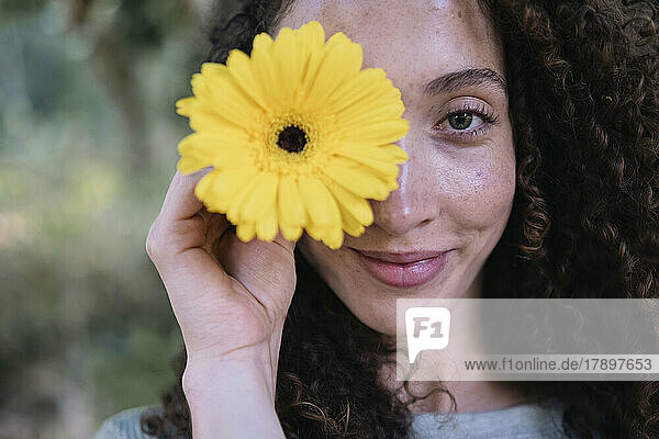 Smiling beautiful woman holding yellow flower over eye
