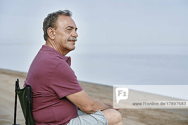 Nachdenklicher älterer Mann sitzt auf einem Klappstuhl am Strand