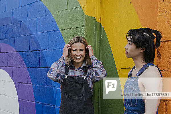 Cheerful woman standing next to man in front of rainbow mural