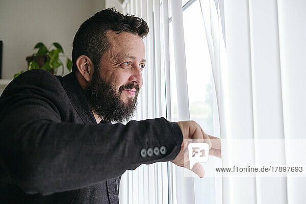 Smiling businessman looking out of window at home