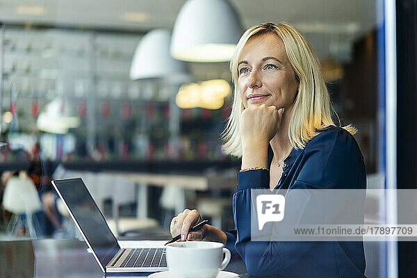 Thoughtful businesswoman with laptop sitting in cafe