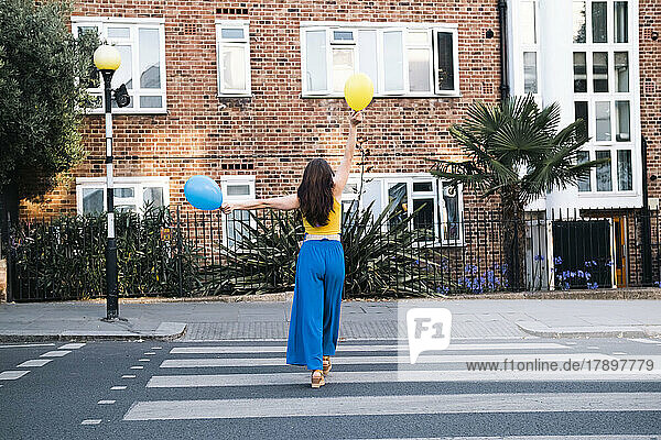 Woman holding balloons walking on zebra crossing in city