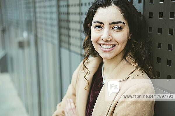 Lächelnde junge Frau im Mantel vor einer Metallwand