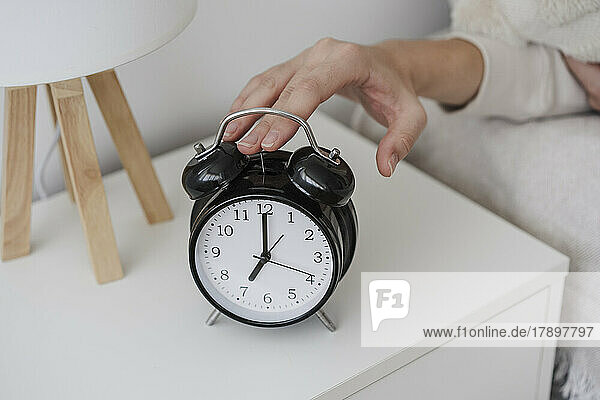 Hand of woman turning off alarm clock on night table