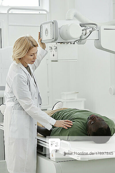 Doctor instructing patient lying on X-ray machine in clinic