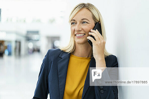 Lächelnde Geschäftsfrau  die am Telefon spricht und sich an die Wand lehnt