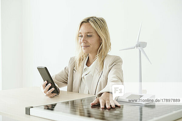 Frau benutzt Mobiltelefon mit Solarpanel und Windturbinenmodell auf dem Schreibtisch