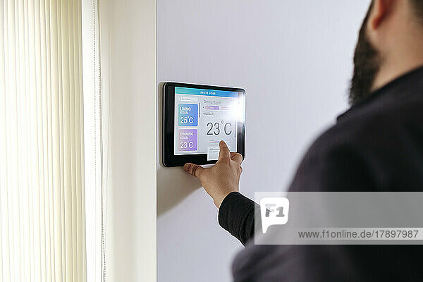 Man adjusting temperature through tablet PC mounted on wall at home
