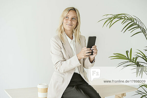 Geschäftsfrau sitzt am Schreibtisch und benutzt Mobiltelefon