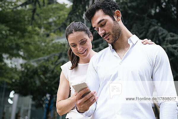 Smiling businesswoman standing by colleague using smart phone