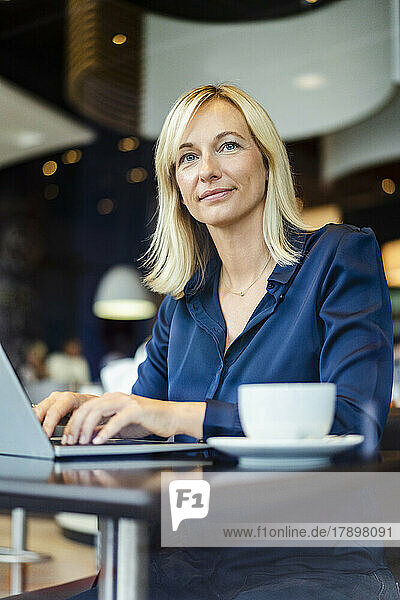 Smiling businesswoman with laptop sitting at table in cafe