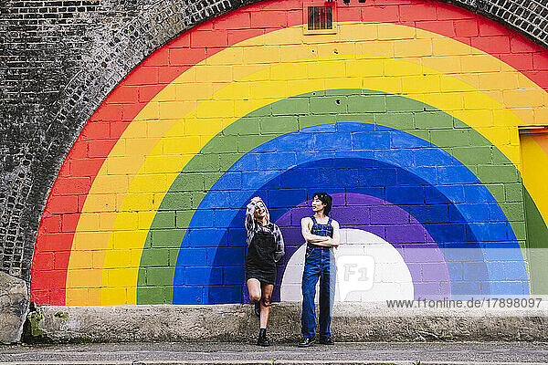 Friends standing together in front of rainbow painted on wall