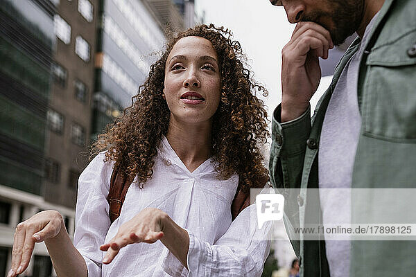 Young woman gesturing and talking with man by building