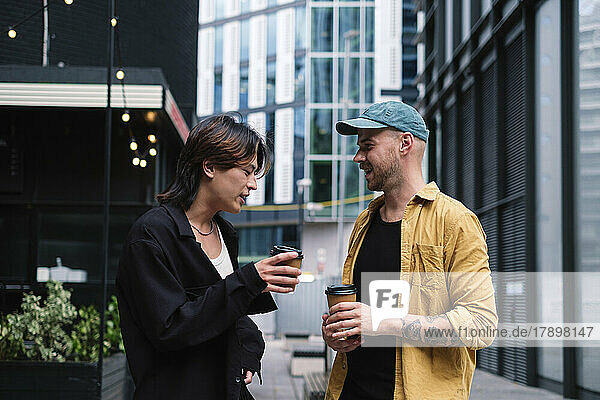 Gay couple with coffee cups talking in front of buildings