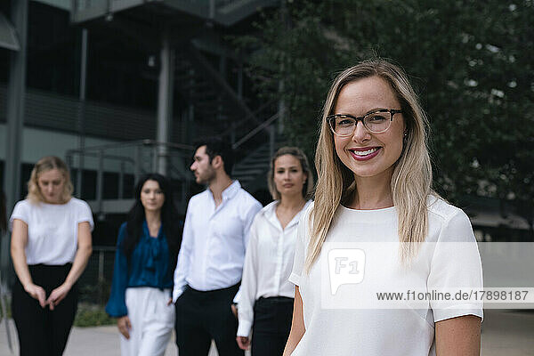 Happy businesswoman wearing eyeglasses standing in front of colleagues at office park