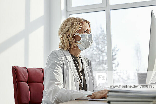 Doctor wearing protective face mask working on desktop PC in clinic