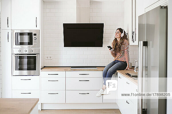 Young woman listening to music with headphones in kitchen at home