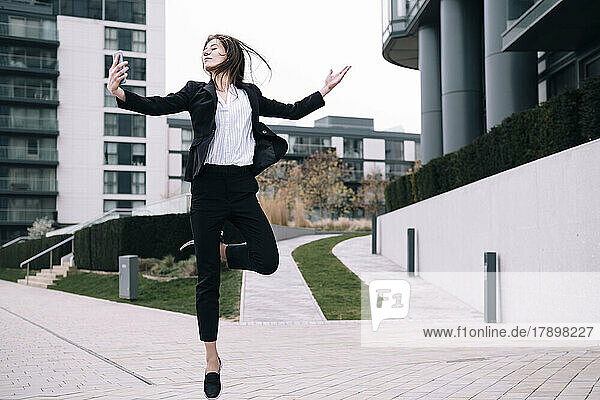 Carefree businesswoman dancing with smart phone outside building