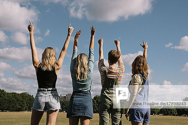Friends with arms raised standing under cloudy sky