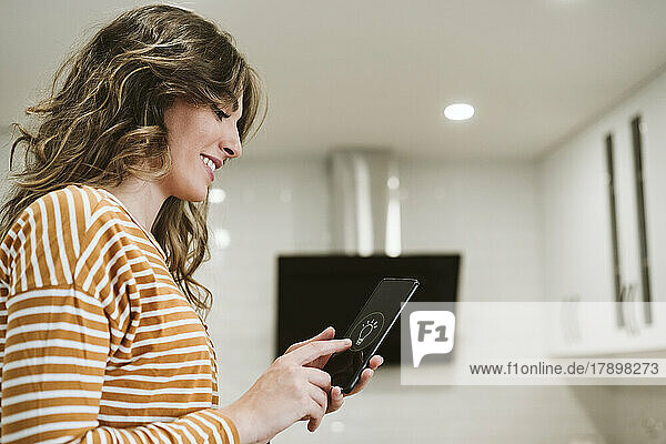 Young woman using mobile phone with smart home app for lighting at home