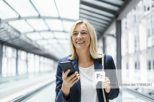 Smiling businesswoman with phone standing on moving walkway