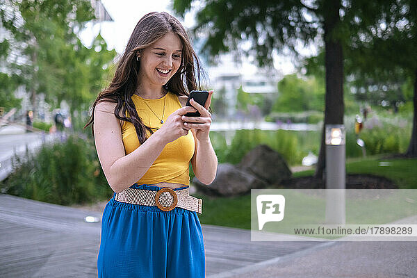 Happy young woman text messaging through mobile phone in park