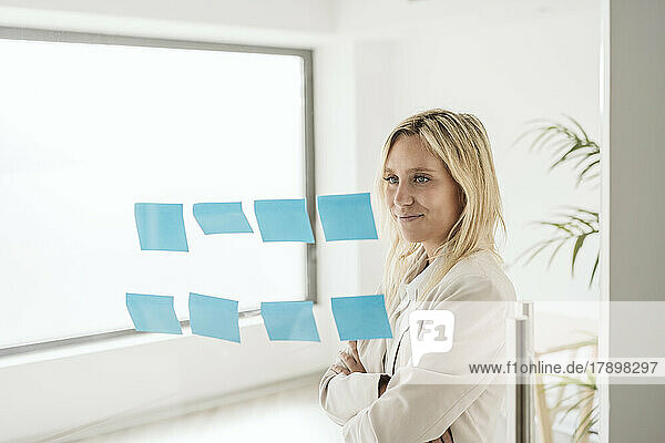 Businesswoman looking at adhesive notes on glass wall in office