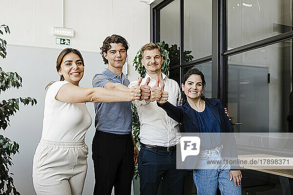 Business people standing together showing thumbs up in office