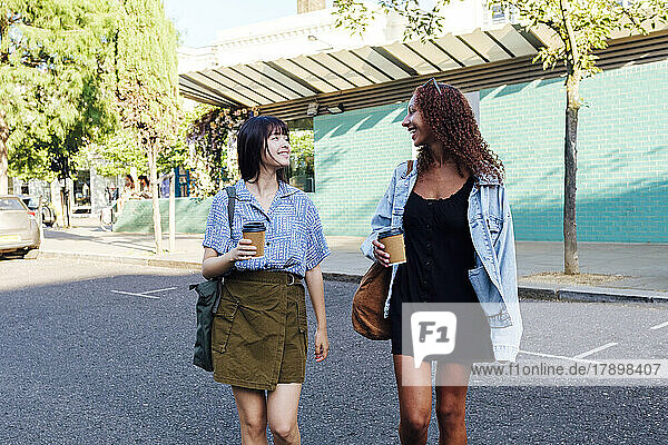Fröhliche Freunde mit einer Kaffeetasse  die auf der Straße spazieren gehen