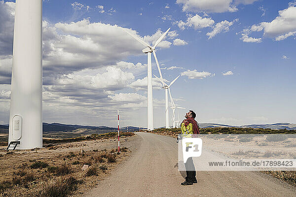 Technician with rope standing on road looking at wind turbine