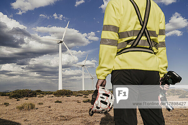 Technician holding work tool and helmet standing at wind farm