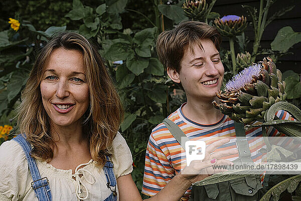 Smiling mature woman by friend looking at flower standing amidst plants