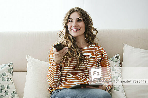 Young woman using remote control on sofa at home