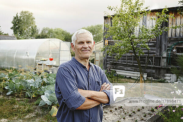 Smiling senior man standing with arms crossed at garden