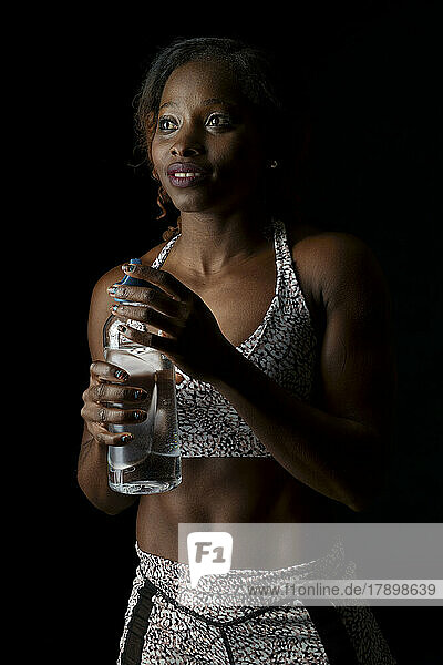 Nachdenklicher Athlet steht mit Wasserflasche vor schwarzem Hintergrund