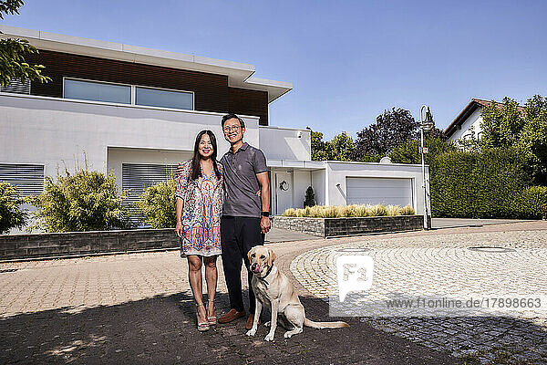 Happy couple with pet dog standing in front of house