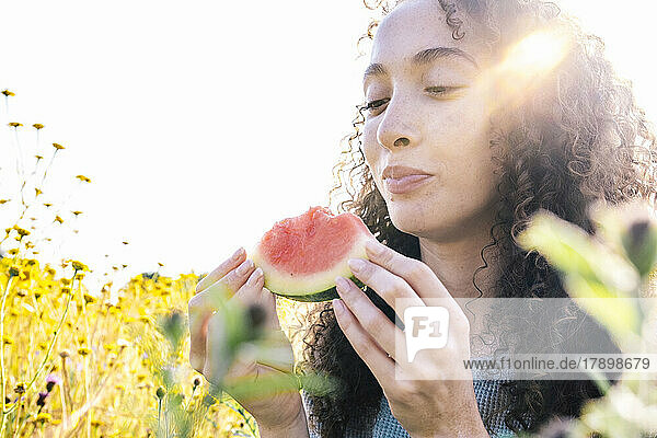 Lächelnde Frau mit Wassermelonenscheibe im Park an einem sonnigen Tag
