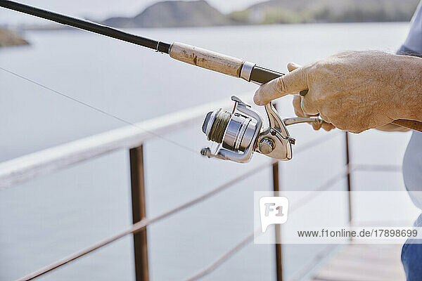 Hand's of senior man with fishing tackle at jetty