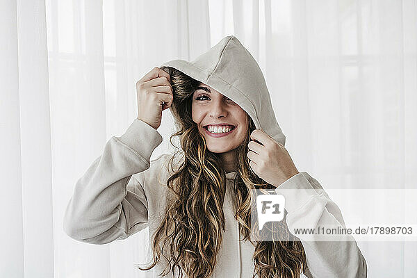 Cheerful young woman wearing hooded shirt at home