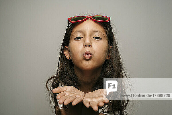 Cute girl with sunglasses blowing kiss against gray background