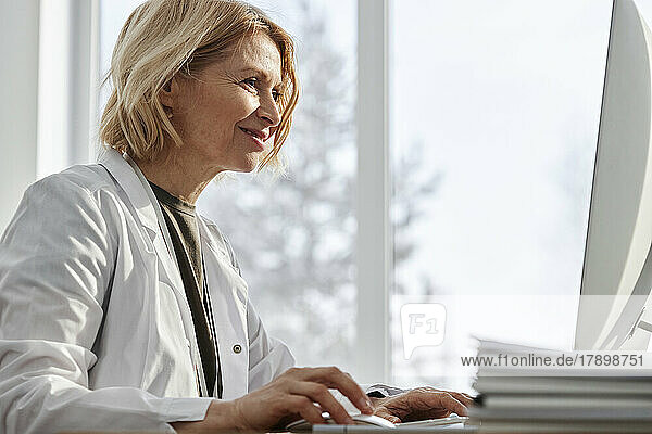 Smiling doctor surfing net on desktop PC in clinic