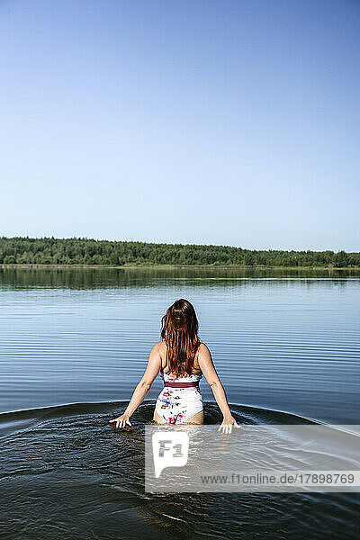 Woman walking in lake under blue sky