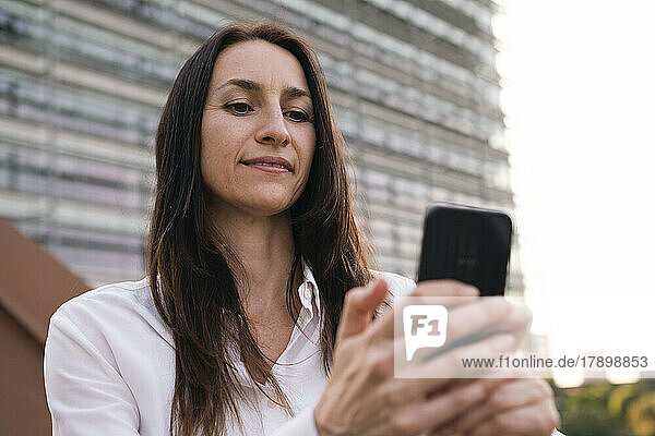 Reife Geschäftsfrau benutzt Smartphone auf Brücke vor Gebäudefassade